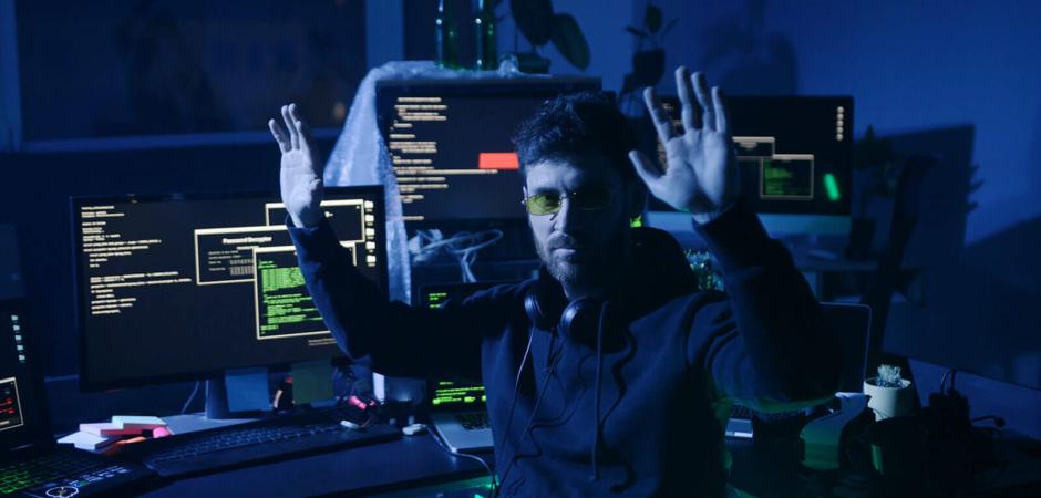 man next to computer with hands in air